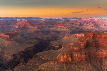 Grand Canyon South Rim at sunrise, golden light on cliffs, deep shadows, colourful sky, dramatic landscape.