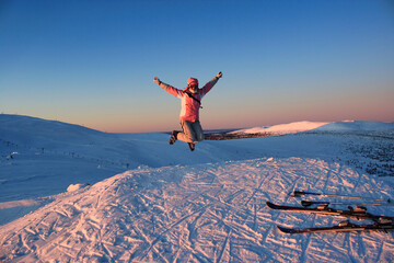Joyful skier in colorful outfit jumping with arms raised on snowy slope at sunrise in Trysil ski resort, Norway. Winter adventure and mountain freedom concept.
