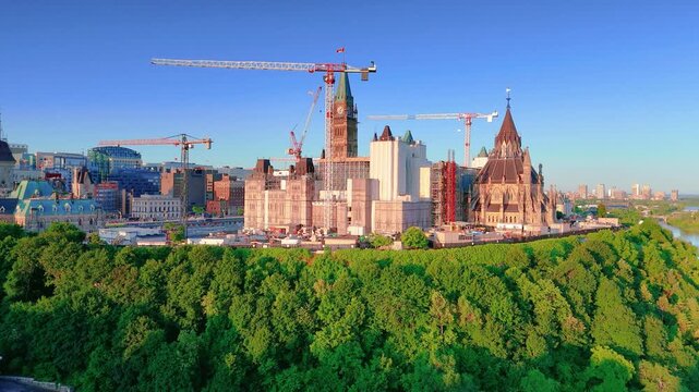 Ottawa, Ontario, Canada. September 25, 2025: Aerial drone view of Canada's Parliament during construction and renovation, showcasing cranes and lush greenery with a clear blue sky backdrop.