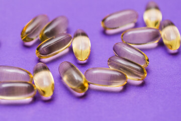 clear yellow Fish oil dietary supplements on purple background 