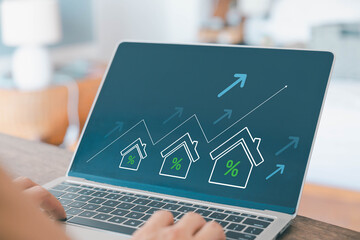 Laptop screen showing house icons with percentage signs and upward arrows, symbolizing real estate...