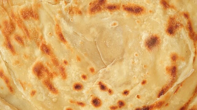 Flaky layers of paratha cooking in a hot pan