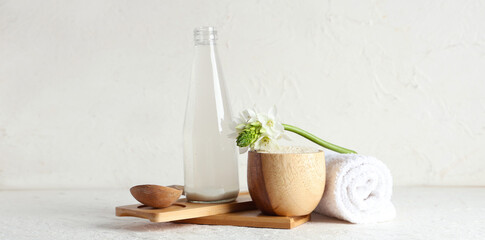 Bottle of natural rice water, grains, flower and clean towel on light background
