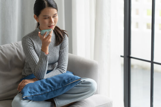 Asian woman using voice assistant on smartphone at home conversation with online assistant Voice chat bot conversational AI Modern Technologies.
