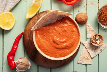 Bowl of tasty muhammara and ingredients on green wooden background
