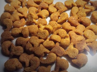 Cat food in the form of small dry grains resembling fish, golden brown in color, arranged randomly on a white surface