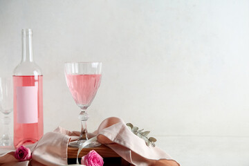 Glass, bottle of pink wine and cloth with roses on table against white background