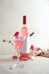Glass and bottle of pink wine with roses on table against white background