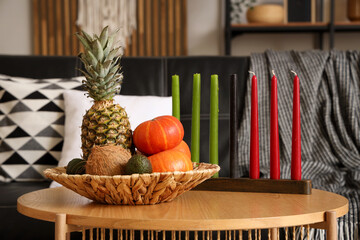 Candles with fruits for Kwanzaa celebration on table in living room, closeup