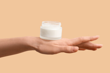 Female hand with jar of cosmetic product on beige background