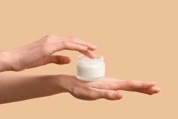 Female hand with jar of cosmetic product on beige background