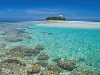 Obraz premium Lush tropical island surrounded by clear turquoise waters and vibrant coral reefs under a bright blue sky