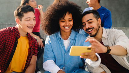 Obraz premium Young multiracial friends smiling and using smartphone outside school college. Youth lifestyle and technology concept
