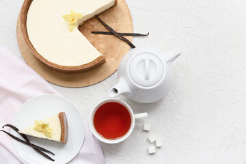 Cut sweet cheesecake with vanilla flowers and cup of tea on white background