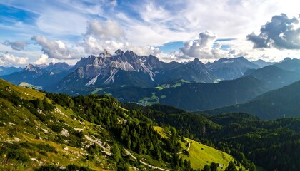 Panoramic view of a mountain range, with lush green valleys and a partly cloudy sky
