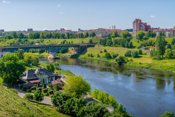 Fototapeta premium Panoramic view of the Neman River in Grodno, Belarus, with Old Bridge, riverside house café and tree-lined embankment on a sunny summer day 