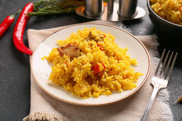 Plate of tasty pilaf with chili peppers and rosemary on black background, closeup
