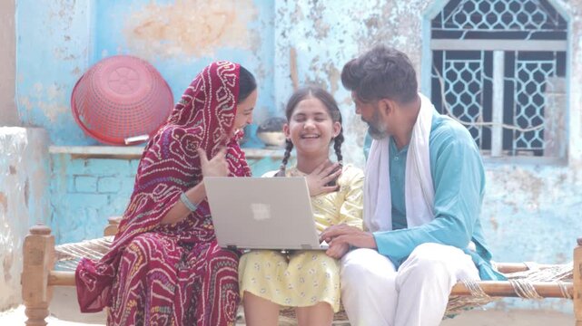Happy rural indian family using laptop. Parents with child daughter learning computer modern technology at home. Girl education. India. 4k