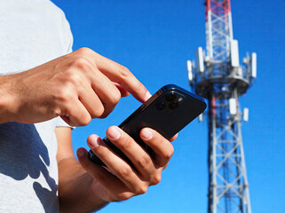 A person is using a smartphone with a telecommunication tower visible in the background, highlighting modern technology and communication.