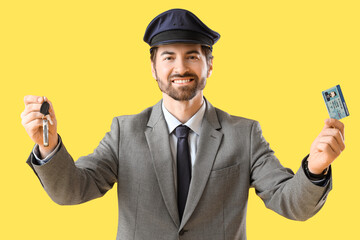Handsome chauffeur with car key and driver's license on yellow background