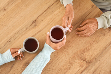 Female caregiver with senior woman drinking tea at table in kitchen, top view