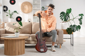 Young man with dreadlocks and electric guitar sitting on sofa at home