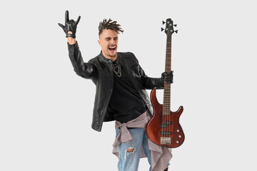 Fototapeta premium Excited young man in a leather jacket and ripped jeans holding a bass guitar and making a rock gesture, the musician expresses joy and enthusiasm, embodying a rock and roll lifestyle