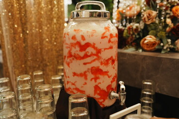 A beverage dispenser with a pink and white drink mixture.