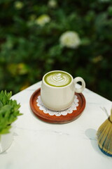 A cup of matcha latte with latte art on a wooden plate.