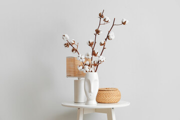 Vase with cotton flowers, wicker box and lamp on table in living room, closeup