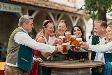 Smiling friends in Bavaria gather at beer garden toasting with mugs of beer enjoying leisure tradition German culture and festive atmosphere