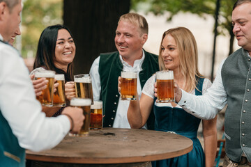 Joyful men and women clinking beer mugs in Bavarian beer garden celebrate leisure tradition friendship Oktoberfest spirit and German culture