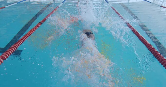 Competitive sports swimmer gripping block and thrusting legs into blue pool for backstroke start