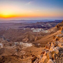 Sunrise over a vast, arid desert landscape, showcasing colorful rock formations and a distant horizon