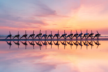 Group of women practicing triangle pose yoga on the beach during sunrise