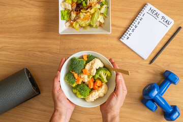 Nutrition plan and healthy eating lifestyle concept with blank weekly diet planner, vegetables, salad, fitness weights and yoga mat for calorie control and balance.