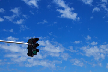 Green Traffic Light Against a Deep Blue Sky with White Clouds