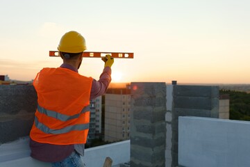 Construction worker using spirit level at building site with crane in background