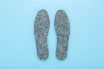New gray soft natural felt insoles on light blue table background. Pastel color. Closeup. Top down view.