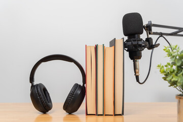 Books with headphones and microphone on wooden desk representing podcast learning audiobook and...