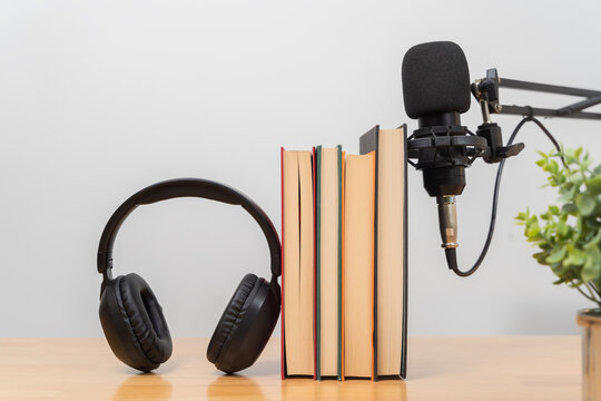 Books with headphones and microphone on wooden desk representing podcast learning audiobook and education