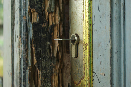 metal lock attached to an old wooden door with peeling paint and a rusty frame