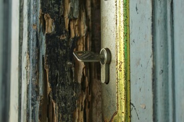 metal lock attached to an old wooden door with peeling paint and a rusty frame