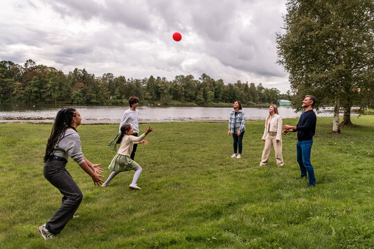 group of people excitedly playing with a red ball on a grassy field.