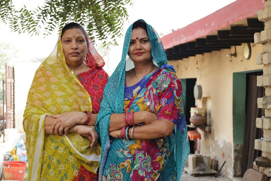 Two happy traditional indian women housewives wearing colorful sari and looking in front of the camera at home in village. Concept of Rural india women empowerment.