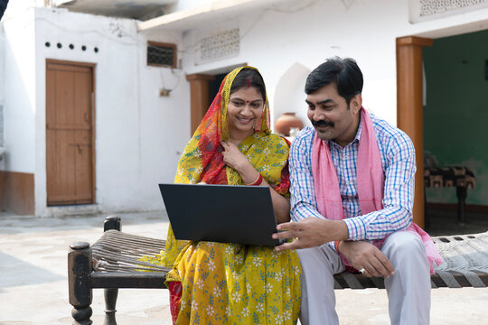 Indian happy rural couple using laptop in village at home. Indian rural middle class couple using technology.