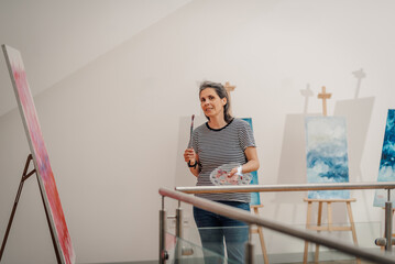 Female artist holding paintbrush and palette, creating abstract art in studio