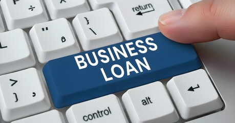 A finger presses a blue "Business Loan" key on a white computer keyboard, emphasizing financial assistance for companies.