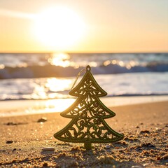 A small, decorative Christmas tree ornament sits on a sandy beach at sunrise or sunset.  Ocean waves gently lap the shore