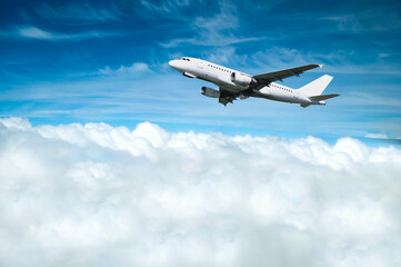 White commercial airplane flying over the clouds high in the blue sky, white airplane in the flight over the land surface among clouds